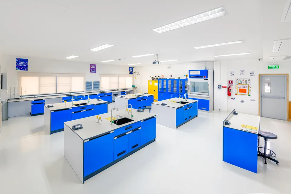 The BCIS science laboratory, with blue lab benches, sinks and gas taps, a fume cupboard and chemical storage