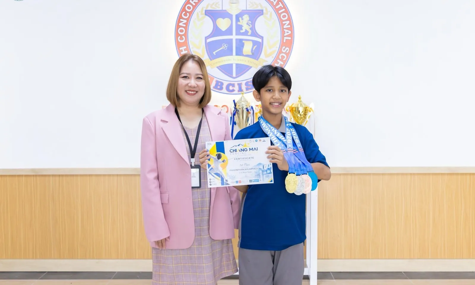 Pluem with his medals and certificate and a member of BCIS staff at school