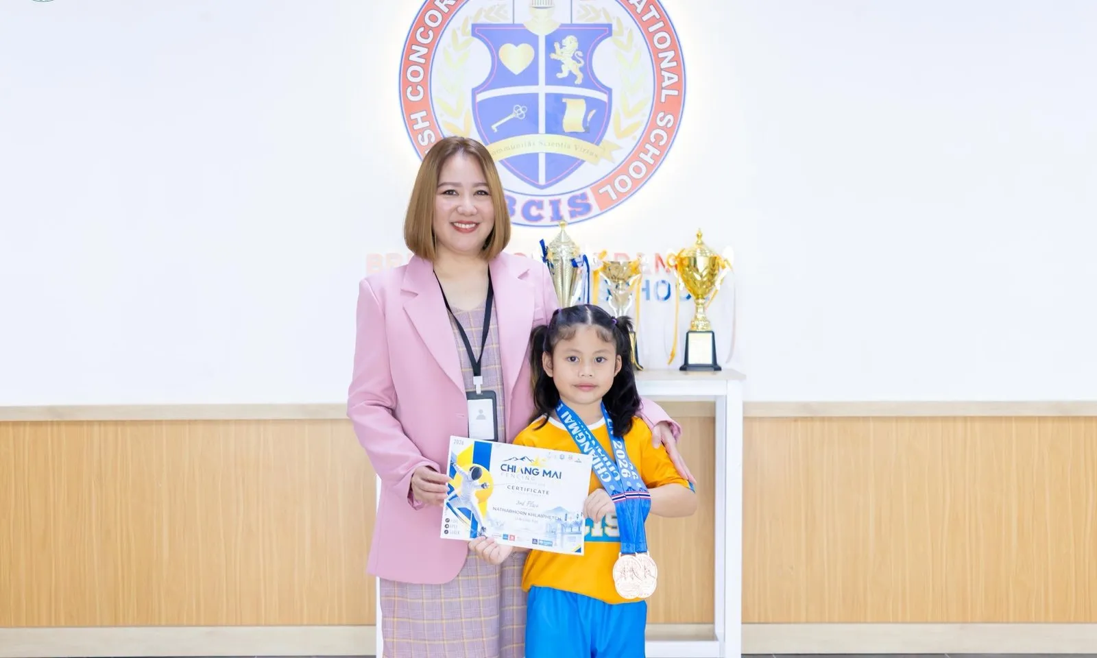 Primprim with her medals and certificate and a member of BCIS staff at school