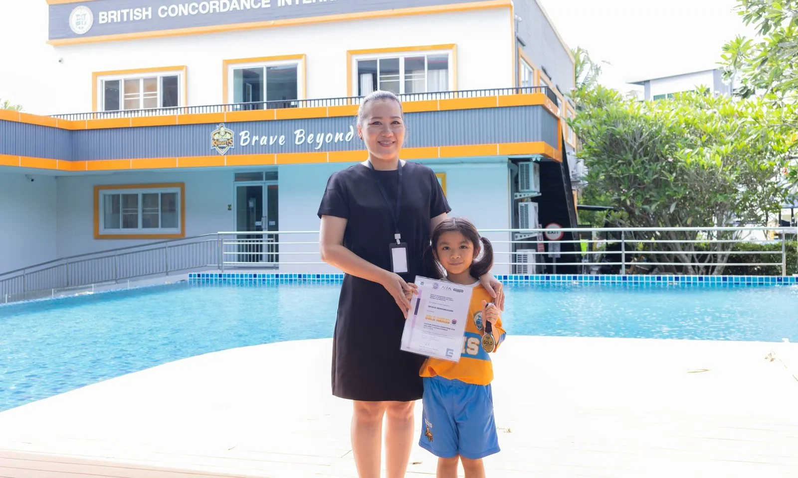 Tubtim with her certificate and a member of BCIS staff beside the school pool