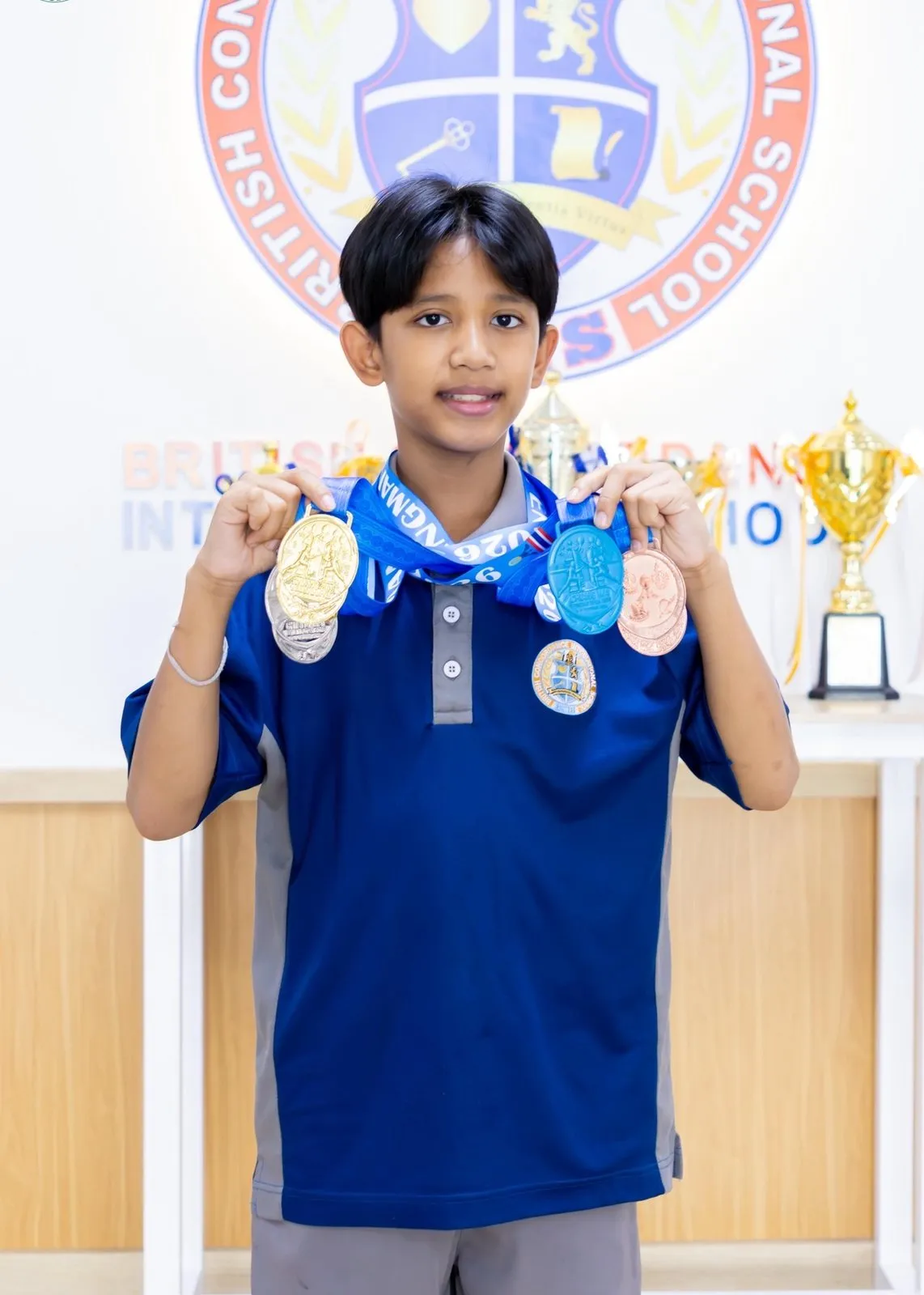 Pluem holding up his medals in front of the BCIS crest