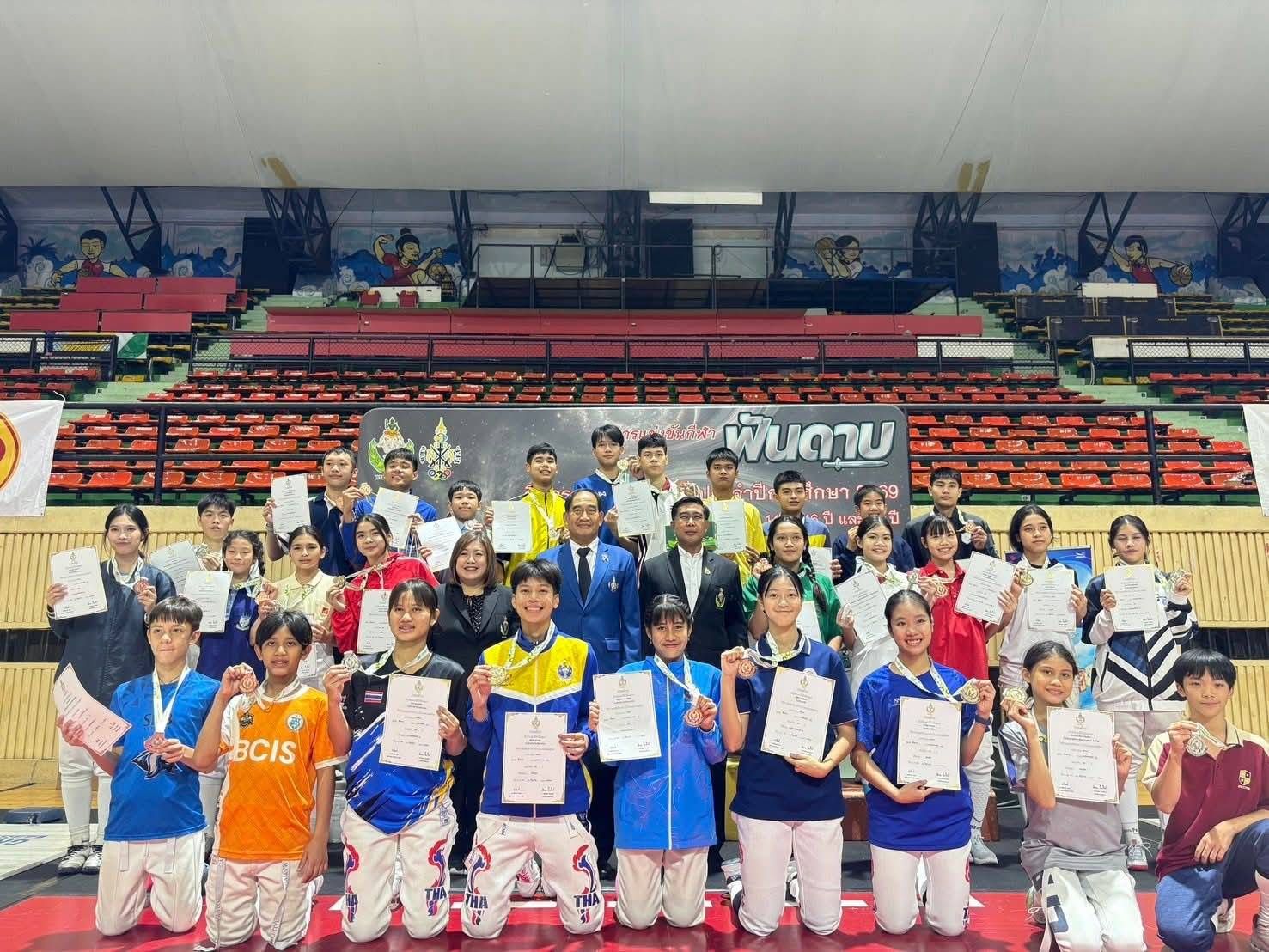 A large group of young fencers and their medals and certificates on stage at the closing ceremony of the National Inter-School Fencing Championship