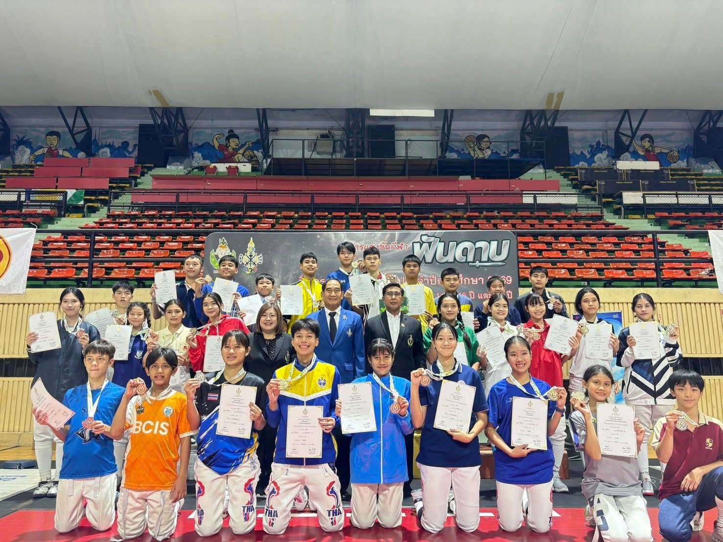 A large group of young fencers and their medals and certificates on stage at the closing ceremony of the National Inter-School Fencing Championship
