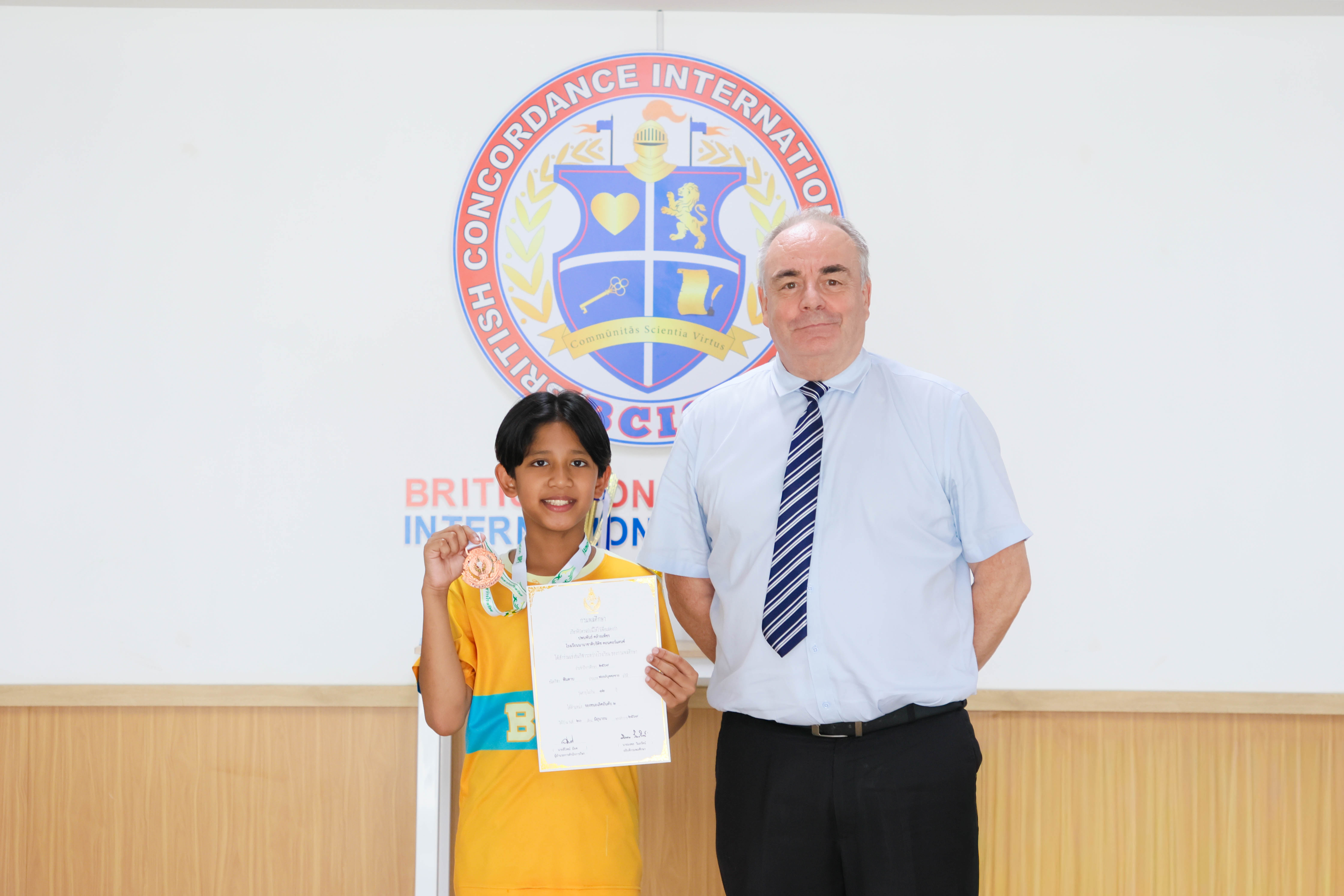 Pleum holding his bronze medal and certificate at school, sharing the moment with a member of the BCIS community
