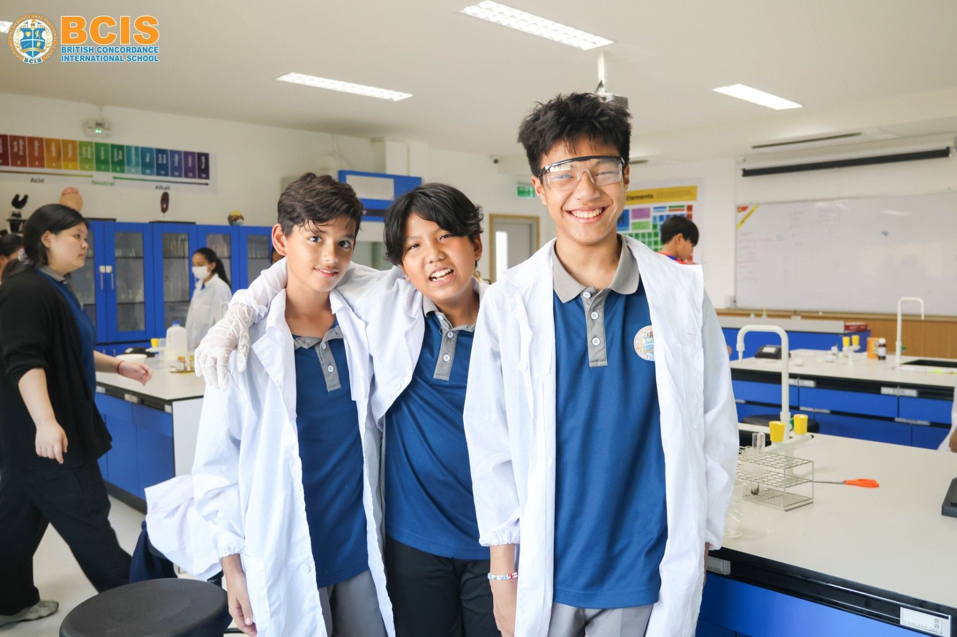 Three BCIS Secondary students in lab coats, smiling in the science laboratory