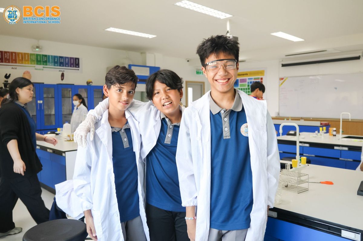 Three BCIS Secondary students in lab coats, smiling in the science laboratory