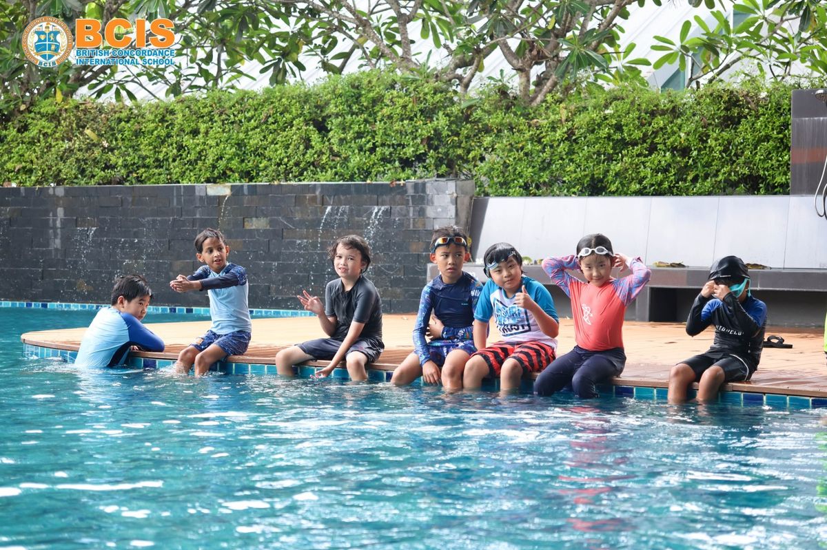 BCIS students sitting on the edge of the school pool during a swimming lesson